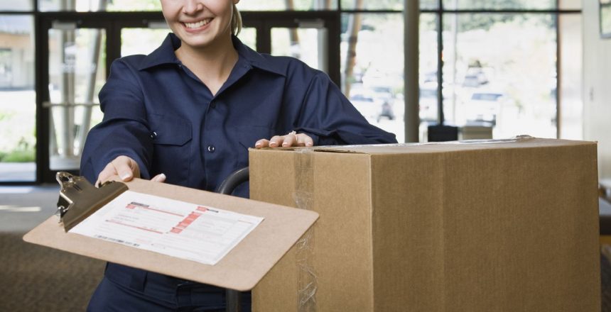 Friendly delivery woman in uniform with stack of cardboard boxes